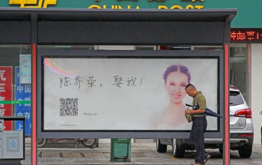 La gente pasa por una parada de autobús con el cartel publicitario "Cásate conmigo", en Xiangyang, provincia de Hubei, el 18 de agosto de 2015.