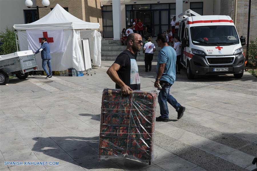 Un hombre carga una cama plegable para las personas afectadas por los incendios forestales, en el Ayuntamiento de Rafina, Grecia, el 26 de julio de 2018. De acuerdo con información de la prensa local, voluntarios se encuentran ofreciendo ayuda luego de los incendios forestales que afectaron asentamientos costeros cercanos a Atenas, con una cifra de al menos 83 personas muertas y 187 heridas hasta el momento. (Xinhua/Lefteris Partsalis)