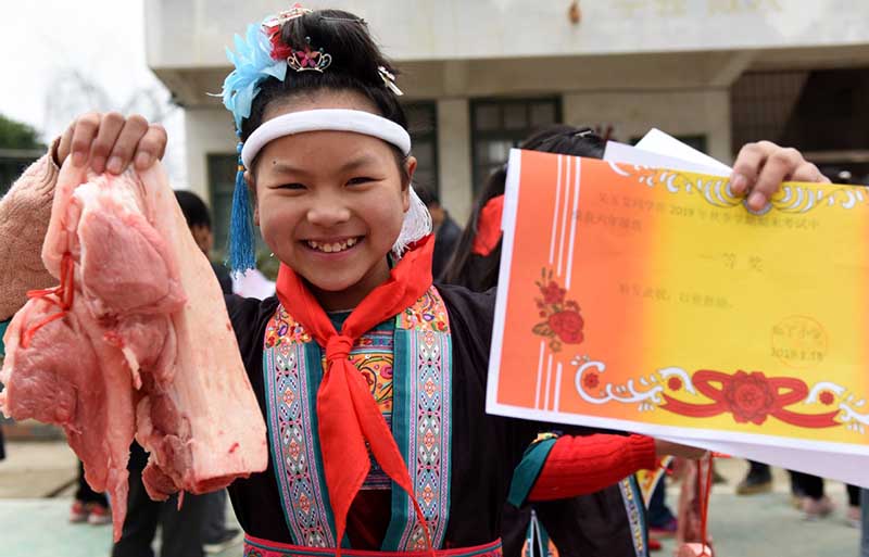 Una estudiante muestra un trozo de carne de cerdo y un certificado obtenido por su buen desempe?o académico-en una escuela primaria de Liuzhou, Región Autónoma Guangxi Zhuang. [Foto: Gong Pukang/ Chinadaily.com.cn]