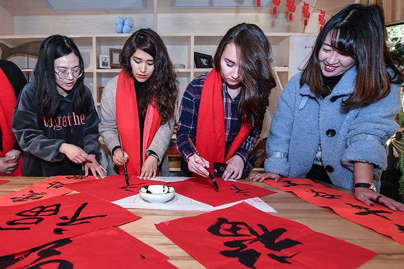 El propietario (a la izquierda) de un hogar que ofrece una habitación en alquiler ense?a caligrafía china a sus huéspedes extranjeros, Hangzhou, provincia de Zhejiang. [Foto: Xinhua]