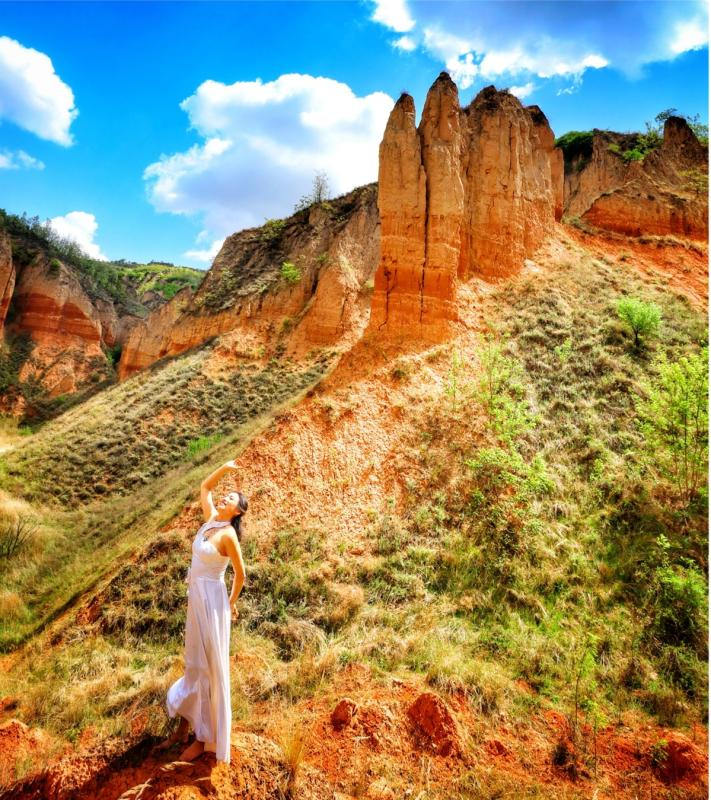 Una turista posa junto a formaciones en el Geoparque de Tierra Roja de Heimapo, Liulin, provincia de Shanxi. [Foto: Wang Fengyun/chinadaily.com.cn]