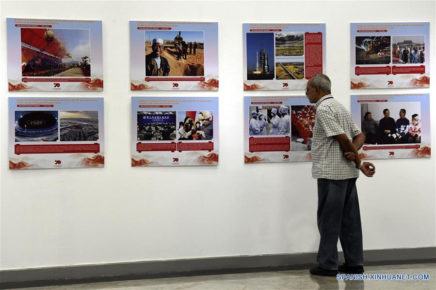 Un hombre observa imágenes de una exposición fotográfica con motivo del 70 aniversario de la fundación de la República Popular China, en la Biblioteca Nacional de Cuba (BNC), en La Habana, capital de Cuba, el 30 de septiembre de 2019. Una exposición que abarca los últimos 70 a?os de historia china se inauguró el lunes en la BNC. (Xinhua/Joaquín Hernández)