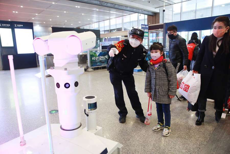 Un policía ayuda a una ni?a a tomarse la temperatura corporal a través de un robot multifunción en la estación de tren norte de Xi'an, capital de la provincia de Shaanxi, noroeste de China, el 7 de febrero de 2020. (Foto de Zhang Xin / Pueblo en Línea)