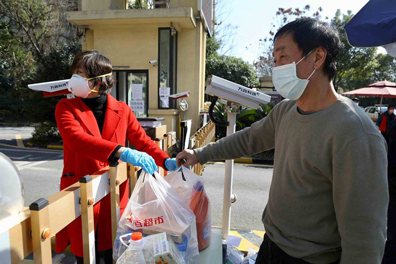 El 18 de febrero del 2020, una mujer compra comestibles en la puerta de una comunidad residencial en Wuhan, provincia de Hubei.?[Foto: Zhu Xingxin / China Daily]