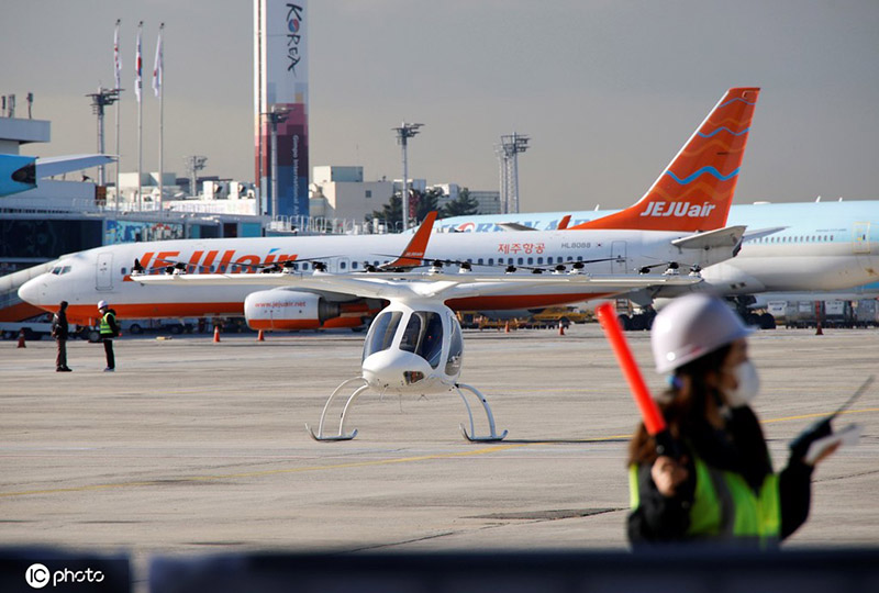 Un empleado del evento hace un gesto frente al taxi aéreo no tripulado "Volocopter 2X" durante un evento de demostración de movilidad aérea urbana en el Aeropuerto Gimpo de Seúl, Corea del Sur, el 11 de noviembre de 2021. (Foto / IC)