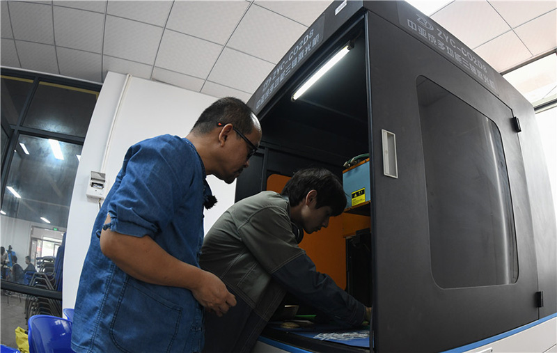 Zhang Bidi (a la izquierda) y su estudiante tallan en coco con una máquina láser en su taller de Qionghai, provincia de Hainan, 18 de febrero del 2022. [Foto: Xinhua]